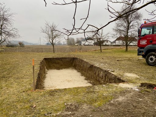 Eine rechteckige Grube in einem offenen Feld, umgeben von Bäumen und einem Lkw.