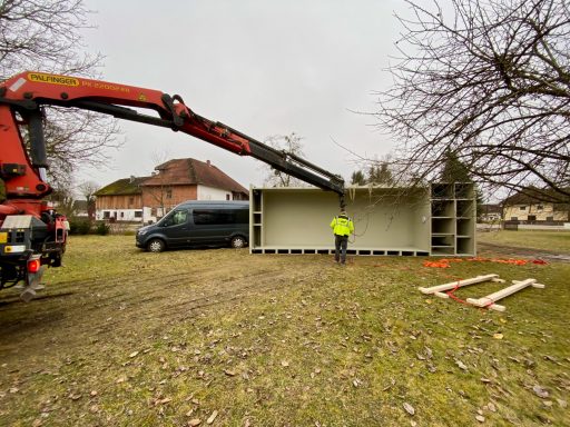 Ein Kran hebt einen Containern, während eine Person in Arbeitskleidung zuschaut.