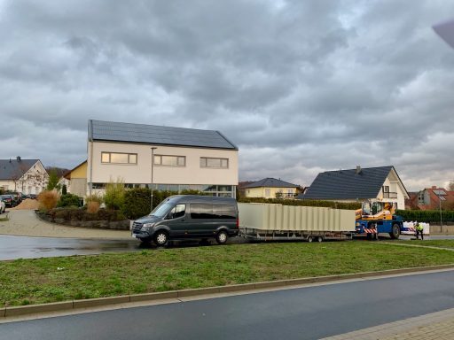 Schwarzer Van mit Anhänger neben Wohnhäusern an einer kurvenreichen Straße.
