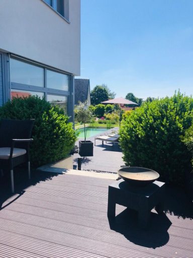 Sonnige Terrasse mit Sitzgelegenheiten und Pool, umgeben von grünen Pflanzen.