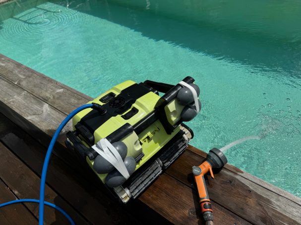 Wasserpumpe auf Holzplattform neben einem Pool, mit einem Schlauch angeschlossen.